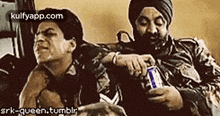 two men are sitting next to each other on a couch . one of the men is holding a can of beer .