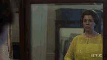 a woman in a yellow dress looks at herself in a mirror with netflix written on the bottom