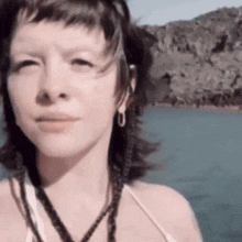 a woman wearing a necklace and earrings is standing next to a body of water .