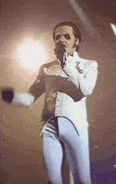 a man in a white suit is standing on a stage with a microphone .