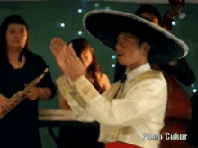 a man wearing a sombrero is clapping his hands in front of a group of people and the words pisau ukur are visible