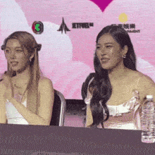 two women are sitting at a table with a bottle of water on it