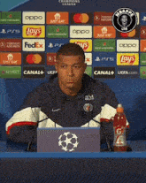 a man sitting at a desk with a bottle of gatorade in front of him and lays advertisements behind him