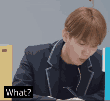 a man in a suit sits at a desk with a sign that says " what "