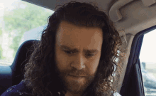 a man with long hair and a beard is sitting in a car