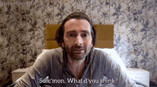 a man with a beard is sitting in front of a bed and says " so c'mon what d'you think "