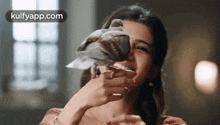 a woman is holding a pigeon in front of her face and smiling .
