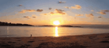 a sunset over a body of water with a person walking on the beach in the foreground