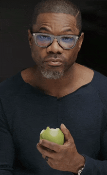 a man wearing glasses is holding a green apple