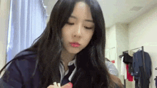 a woman with long black hair is applying lipstick in a room .