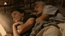 a man and a woman are laying in bed with the letter a on the bottom right