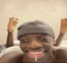 a man wearing a beanie is laying on a bed with his feet up and his mouth open .