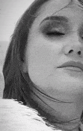 a black and white photo of a woman 's face with her eyes closed and her hair blowing in the wind .
