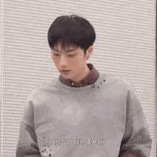a young man wearing a grey sweater and a brown shirt is standing in front of a white wall .