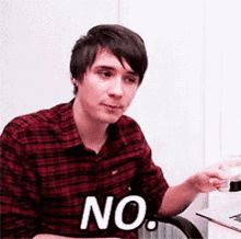 a young man in a plaid shirt is sitting at a desk and says no .