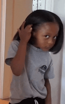 a little girl in a gray shirt is holding her hair .