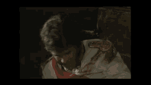 a man in a military uniform with a red sash is sitting in a dark room .