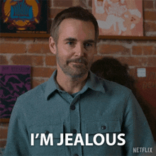 a man in a blue shirt says i 'm jealous in front of a brick wall