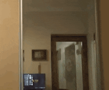 a person is standing in front of a mirror in a hallway with a tv on the wall .