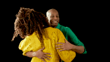 a man in a green shirt and a woman in a yellow sweater are hugging