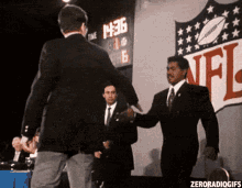 two men shaking hands in front of a nfl sign