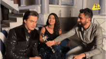 two men and a woman are sitting on a couch with a microphone and a sign that says biz asia on it