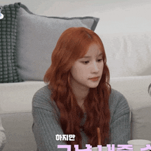 a woman with red hair is sitting on a couch with korean writing on the bottom
