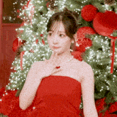 a woman in a red dress stands in front of a decorated christmas tree