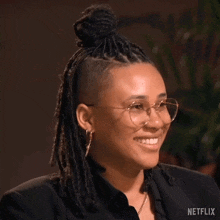 a woman with dreadlocks and glasses is smiling and wearing a black shirt .