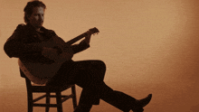 a man sitting on a chair playing a guitar