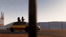 two women are standing on the back of a yellow car
