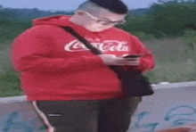 a man in a red coca cola hoodie is using a cell phone .