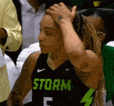 a female basketball player wearing a storm jersey holds her hand to her head .
