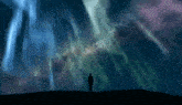 a man standing on top of a hill looking at the aurora borealis .