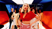 a woman in a red crop top and plaid skirt is dancing with a group of women
