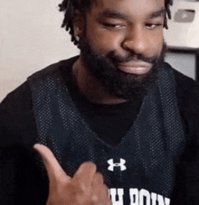 a man with a beard is wearing a black under armour jersey and giving a thumbs up .