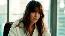 a woman in a white coat is sitting in front of a window .