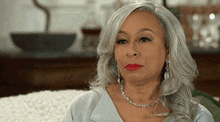 a woman with gray hair and red lipstick is wearing a silver necklace and earrings