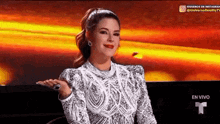 a woman in a white dress is sitting in front of a red background and making a funny face .