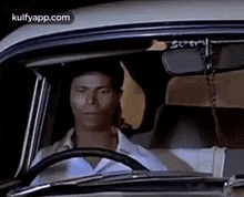 a man is sitting in the driver 's seat of a car looking out the window .