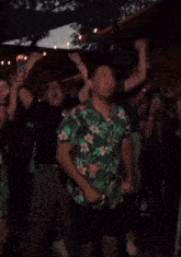 a man wearing a green shirt with flowers on it is dancing in a crowd