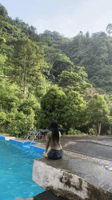 a woman sits on the edge of a pool in front of a forest