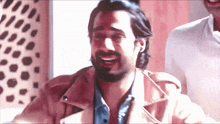a man with a beard is smiling and wearing a tan leather jacket