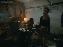 a woman is standing in front of a drum set in a garage with the words terasgifs written above her