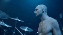 a shirtless man playing drums in a dark room