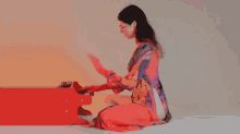 a woman in a colorful dress is kneeling down playing a red piano .