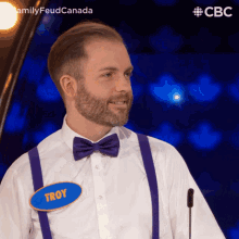 a man wearing purple suspenders and a bow tie has a name tag that says troy