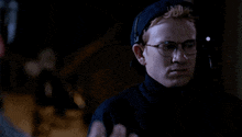 a man wearing glasses and a baseball cap is standing in the dark .