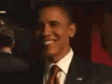 barack obama is smiling and looking at the camera in a suit and tie .