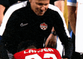 a man wearing a black canada shirt talks to a player wearing a red number 23 jersey